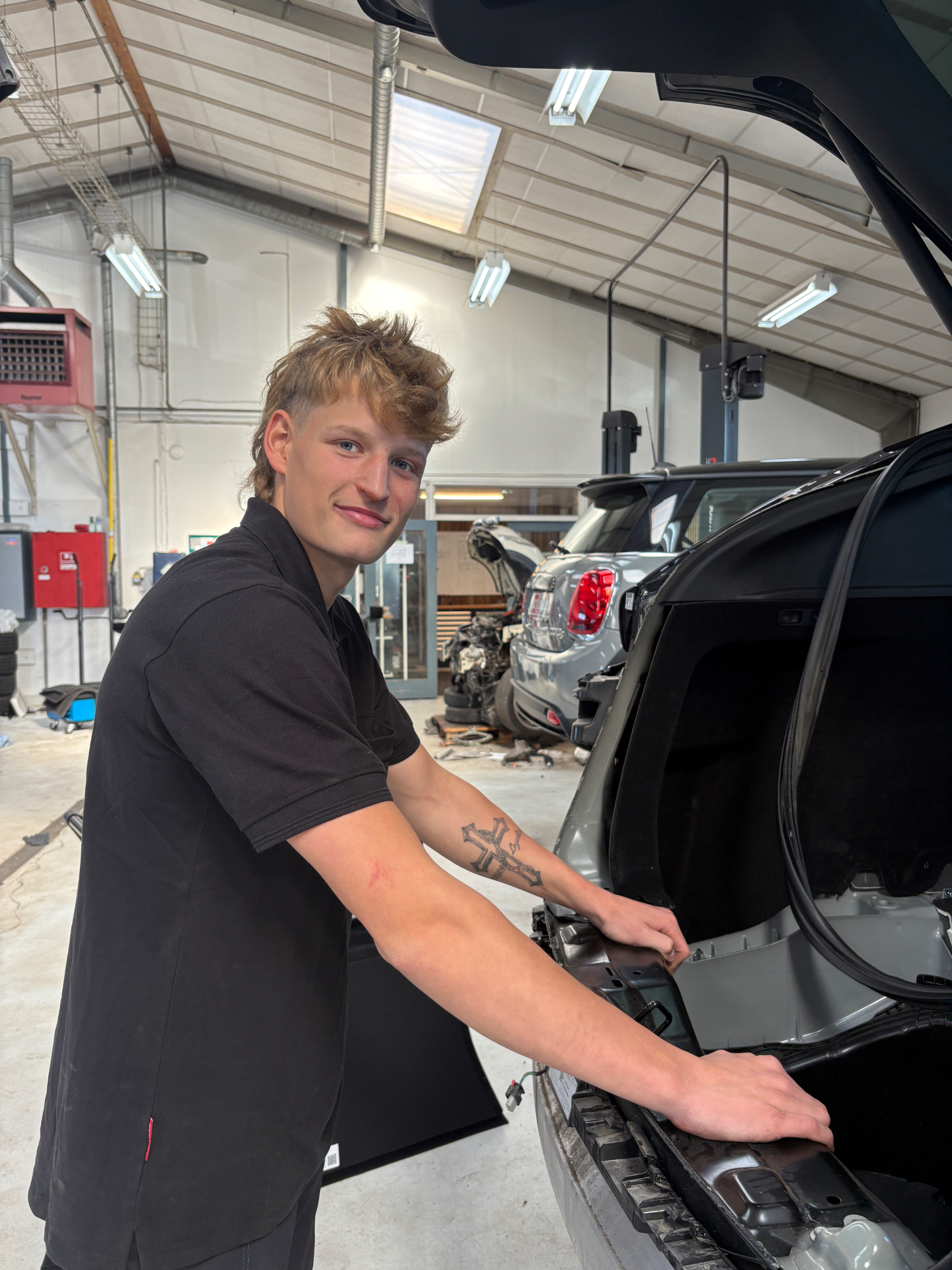 Jacob Pedersen, værkstedsmedhjælper hos CC Biler, ved en bil med åben bagklap i værkstedet